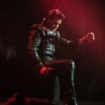 Elvis impersonator JD King kneeling on stage in black leather